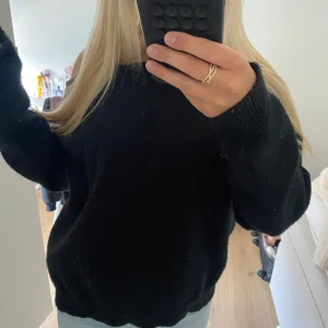 Svart offshoulder stickad tröja - Mysig svart stickad tröja med offshoulder-look och lång ärm. Tröjan har en loose passform och är perfekt för dig som gillar en avslappnad och trendig stil. Passar till jeans eller kjol för en chill vibe.