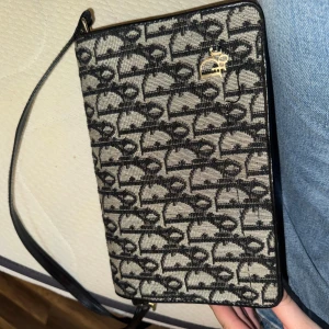 Vintage Christian Dior svart axelväska - Snygg axelväska från Christian Dior med klassiskt monogrammönster i svart och beige tyg på framsidan och slät svart skinnbaksida. Väskan har guldfärgad logga, justerbar axelrem och flera fack med dragkedja inuti. Har inget intyg på att väskan är äkta förutom stämpeln, då den är gammal från ungefär 1970 talet.  Väldigt fint skick och som gott oanvänd!