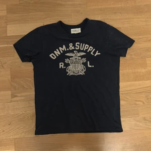 Denim and supply T-shirt - Säljer en mörk blå t-shirt från denim and supply med tryck 'Denim & Supply' på framsidan. T-shirten har en klassisk rund hals och korta ärmar. Perfekt för en avslappnad stil.
