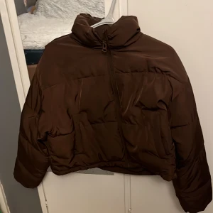 Brun pufferjacka från H&M Divided - Säljer en brun pufferjacka från H&M Divided i storlek S. Jackan har hög krage, dragkedja framtill och en riktigt chill oversized vibe. Perfekt för kalla dagar när du vill vara både varm och snygg. Materialet är syntet och jackan är quiltad för extra värme.