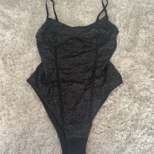Svart spetsbody från hm  - Supersnygg svart body från hm med tunna axelband och blommig spets över hela framsidan. Figurnära passform och markerade sömmar ger en riktigt trendig look. Perfekt att styla med jeans eller kjol för en cool outfit.