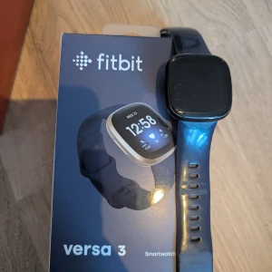 Fitbit Versa 3 smartwatch blå - Säljer en Fitbit Versa 3 smartwatch med fyrkantig urtavla och blått silikonarmband. Klockan har en stilren design och passar perfekt för dig som vill hålla koll på träning, steg och puls direkt på handleden. Repig skärm men är nog inga problem att polera bort alt byta skärm som tanken var att göra själv.