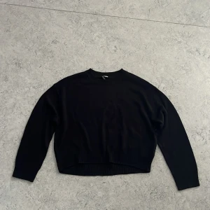 Svart stickad tröja från H&M Divided - En svart stickad tröja från H&M Divided i storlek S. Tröjan har rund halsringning, lång ärm och ribbade muddar vid ärmslut och nederkant, även lite kortare nederkant fram. Enkel och clean design som är lätt att matcha med allt. Lite knottig från att ha blivit tvättad ett par gånger, annars inga defekter.