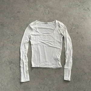 Vit långärmad topp med rund hals - En basic vit långärmad topp med rundad, lite djupare urringning. Tunt och mjukt material som känns skönt mot huden. Perfekt att styla med jeans eller kjol för en clean look. Slit på båda ärmarna så de går över handen, men inte sitter åt. Har klippt bort lappen, men tröjan är storlek S från Gina tricot. Inga defekter, endast tvättad.