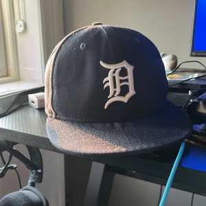 Detroit Tigers keps New Era 59FIFTY - Säljer en klassisk svart Detroit Tigers keps från New Era 59FIFTY-serien. Kepsen har en rak skärm och broderad vit D-logga framtill samt MLB-logga bak. Tillverkad i ullblandning för en autentisk look. Perfekt för dig som gillar streetwear och sport.