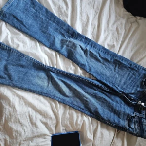 Blå bootcut jeans från Gina Tricot - Snygga blå jeans från Gina Tricot i klassisk bootcut-modell. Jeansen har normal passform, fem fickor och coola broderade detaljer på bakfickorna. Tillverkade i mjukt denim med dragkedja och dubbla knappar framtill. Fint skick!