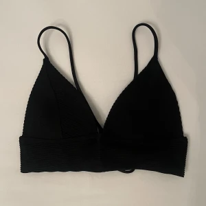 Svart ribbad bikini H&M - Svart bikini från H&M med ribbad struktur och smala axelband. Toppen har trekantsformade kupor och knytning i ryggen för en snygg passform. Vaddering med lätt push-up. Passar dig med A-kupa. Säljs då den inte kommer till användning längre 