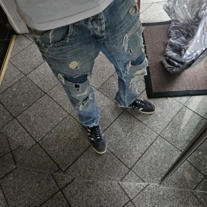 Blå slitna straight fit jeans - Riktigt snygga ljusblå jeans med massor av slitningar och hål för en rå streetstil. Modellen är rak och byxorna har klassiska fem fickor. Pris går att diskutera vid snabb affär.