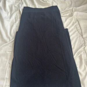 Svart ribbad långkjol - En svart långkjol med ribbad struktur. Kjolen har en enkel och stilren design med hög midja och rak passform. Perfekt att matcha med en crop top eller oversized hoodie för en chill look.