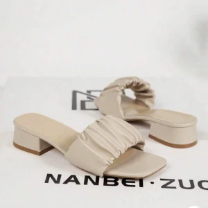 Beige sandaler med låg klack -  beige sandaler med fyrkantig tå och låg klack. Skorna har en bred, rynkad rem över foten och är tillverkade i syntetmaterial.