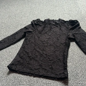 Svart spetsblus från Lindex XS - Supersnygg svart blus från Lindex i storlek XS, med blommig spets. Långärmad modell med lätt puff vid axlarna. Ganska genomskinlig det ser man om man jämför med min hand. Fint skick