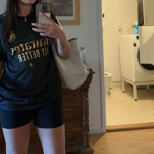Real Madrid Bellingham svart tröja - Snygg svart Real Madrid fotbollströja från Adidas med guldiga detaljer och tryck. På bröstet finns klubbmärket och sponsorlogga, på ryggen står det Bellingham och nummer 5. Klassisk passform med korta ärmar och rund hals. Perfekt för dig som älskar fotboll och vill sticka ut.