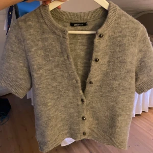 Grå kofta från Gina Tricot - Mysig och söt grå kofta från Gina Tricot med korta ärmar och rund halsringning. Koftan är stickad i ett mjukt material och har knappar framtill. Superfin att ha över ett vitt basic linne!❤️ Hör av er vid frågor!❤️ Pris går att diskutera❤️
