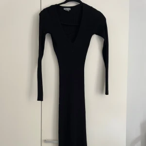 Svart ribbad långklänning Lindex - Svart långklänning från Lindex med ribbad struktur och v-ringad hals. Klänningen har lång ärm och sitter tight mot kroppen för en snygg siluett. Perfekt för dig som gillar stilrena och enkla plagg med en modern touch.
