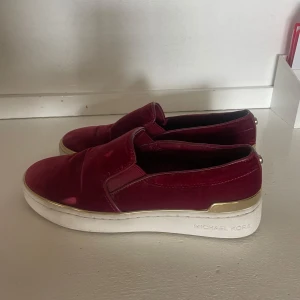Röda slip ons i sammet - Röda slip ons i sammet från Michael Kors. Har två små fläckar på vänstra skon som man ser på bilden 
