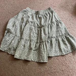 Grönblommig volangkjol - Supersöt grön kjol med ett blommönster och flera volanger. Resår i midjan för skön passform och flowig känsla. Använd fåtal gånger 