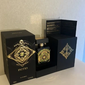 Initio Black Gold Oud For Happiness 90ml - Lyxig parfym från Initio, Black Gold Project Oud For Happiness, 90ml. Flaskan är svart med detaljer i guld och grönt, prydd med ett mystiskt öga och ornamentik. Fyrkantig form med exklusiv guldfärgad topp och elegant förpackning. Perfekt för dig som gillar unika och djärva dofter.