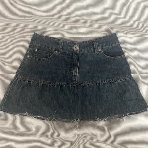 Mörk jeanskjol från KappAhl - Snygg mörkblå jeanskjol från KappAhl i kort modell med rå kant nertill. Kjolen har klassiska fickor fram och bak, bälteshällor och coola sömdetaljer på bakfickorna. Perfekt för dig som gillar en avslappnad och trendig stil.💗kjolen var innan längre men har klippt av längst ner för att få den lite kortare