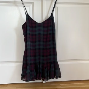 Rutig klänning från Ralph Lauren  - Supersöt kortklänning med tunna justerbara axelband och volangkant nertill. Klänningen har ett rutigt mönster i vinrött, blått och svart, och är fodrad med ett mjukt innerfoder.