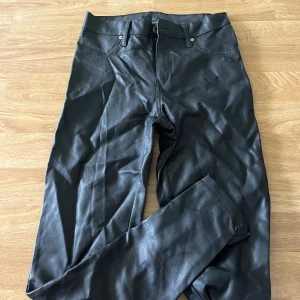 Svarta skinnbyxor med raka ben - Snygga svarta byxor i skinnimitation med klassisk femficksdesign och raka ben. Byxorna har bälteshällor, dragkedja och knapp framtill samt bakfickor. Perfekta för en edgy look och passar till allt.