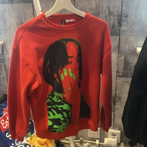 Röd Billie Eilish sweatshirt -  röd sweatshirt med stort tryck av Billie Eilish på framsidan och hennes namn i grönt på ryggen. Tröjan har rund hals och långa ärmar. Jätte skön och super fin!