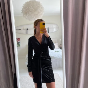 Svart omlottklänning från Bik Bok - Supersnygg svart kort omlottklänning från Bik Bok i sammetsliknande material. Klänningen har lång ärm, markerad midja med knytdetalj och v-ringning. Bältet går att ha hängande om man vill. Aldrig använd, som ny.