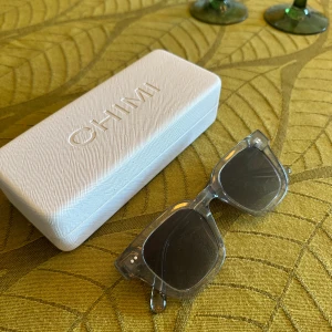 Grå transparenta solglasögon CHIMI - Snygga solglasögon från CHIMI med transparent grå båge och mörka glas. Rektangulär form som ger en cool vibe och passar till många stilar. Kommer med originalfodral i vitt. Perfekta för att lyfta din look i sommar.