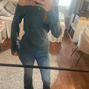 Grön offshoulder tröja från Mohito - Mysig grön tröja från Mohito med offshoulder-modell. Tröjan har långa ärmar, bred ribbad mudd nertill och vid ärmslut. Perfekt för dig som gillar en avslappnad men ändå trendig look.