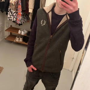 MörkGrå väst från Chevalier - Säljer en snygg grå fleeceväst från Chevalier med dragkedja och broderad detalj på bröstet. Västen har en mysig fleecefoder och är perfekt för kyligare dagar. Den har två praktiska fickor med dragkedja.