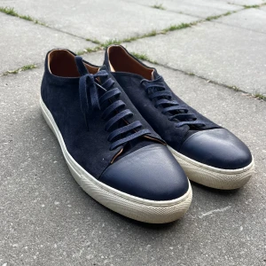 Human Scales - Herbert Suede - Snygga mörkblå sneakers med ovandel i mocka och tåparti i slätt skinn. Skorna har vita, platta sulor och klassisk snörning. Insidan är fodrad i brunt läder för extra komfort. Perfekta för dig som gillar stilrena och tidlösa sneakers. Knappt använda.