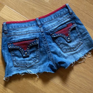 Lågmidjade jeansshorts  - Snygga blå jeansshorts från Vero Moda med röd kant och coola nitar på fickorna. 