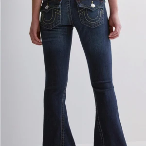True religion jeans  - Snygga mörkblå bootcut jeans med markerade kontrastsömmar och stora bakfickor med dekorativa detaljer. Jeansen har klassisk femficksdesign och är tillverkade i ett stretchigt denimtyg som sitter skönt och formar sig efter kroppen. Kan byta mot ett par ljus blå true religion i samma storlek.