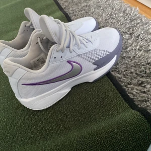 Nike sneakers vit/blå Air Zoom 38 - Nike sneakers i vitt med lila och silverfärgad swoosh. Modellen har mesh- och syntetmaterial, snörning och grå detaljer på sidorna. Snygg sportig look med Air Zoom-dämpning och låg profil. Perfekta för dig som gillar stilrena och coola träningsskor.