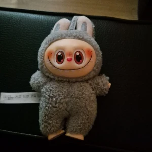 Grå mjukisdocka - Bilderna visar en söt och unik mjukisdocka med stora ögon och grå pälsdräkt.