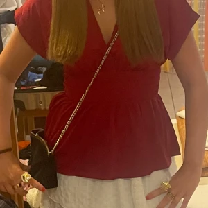 Vinröd omlottopp med v-ringning - Snygg vinröd topp med omlott-design och v-ringning. Modellen har korta ärmar och markerad midja som ger en feminin siluett. Perfekt att styla med jeans eller kjol för en trendig look.