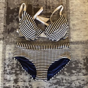 Randig bikini från Panos Emporio - Snygg bikini från Panos Emporio med marinblå och vita ränder. Överdelen (stl. 42) har vadderade kupor och knyt i nacken, medan underdelen (stl. 38)  är högmidjad för en retrovibe. Perfekt för strandhäng och poolparty!
