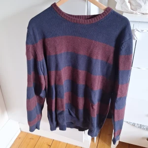 Randig stickad tröja Dressmann L - Säljer en stickad tröja från Dressmann i storlek L. Tröjan har breda marinblå och vinröda ränder, rund halsringning och ribbade muddar. Perfekt för dig som gillar en klassisk men chill stil.