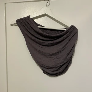 Mörkgrå oneshoulder topp från SHEIN - Säljer en mörkgrå oneshoulder topp från SHEIN i storlek S. Toppen har draperad design och är ärmlös på ena sidan, vilket ger en cool och trendig look. Perfekt för dig som gillar att sticka ut med asymmetriska plagg.