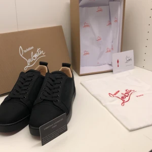 Svarta sneakers från Christian Louboutin - Snygga svarta sneakers från Christian Louboutin med ikonisk röd sula. Skorna har klassisk snörning, rund tå och är tillverkade i tyg med detaljer i skinn. Perfekta för dig som vill ha en stilren och lyxig look med en touch av attityd.