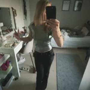 Silvrig t-shirt med öppen rygg - Säljer en glansig silvrig croppad topp med korta ärmar och riktigt snygg öppen rygg. Perfekt för dig som vill sticka ut och gillar futuristisk stil. Sitter tight och har en cool metallic-look som verkligen syns.