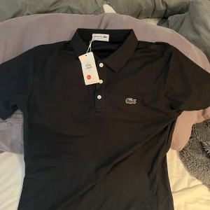 Svart pikétröja från Lacoste - Snygg pike. Den är i nyskick har hängt tillbaka alla tags så de följer med. Köpt i Frankrike.