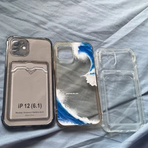 3 iPhone 12 skal med vågmotiv och kortfack - Säljer tre skal till iPhone 12 (6.1 tum). Två är transparenta med inbyggt kortfack och ett har ett snyggt blåvitt vågmotiv. Alla är gjorda i tålig plast och skyddar mobilen samtidigt som de ser stilrena ut. Perfekt för dig som vill ha både funktion och cool design.
