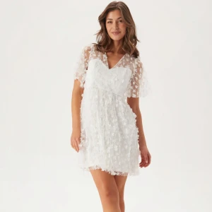 Vit blommig kortklänning med spets - Superfin vit kortklänning med v-ringning och transparenta ärmar. Klänningen har ett blommigt spetsmönster över hela och en lätt utsvängd kjol. Perfekt för sommarens alla tillfällen och ger en romantisk vibe. Perfekt för dig som vill vara unik! 😍🤩✨🌸 Nypris: 999 kr. 