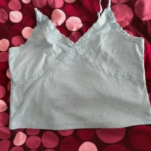 Ljusgrå ribbad linnetopp med spets - Supersöt ljusgrå ribbad linnetopp med tunna axelband och spetsdetaljer längs v-ringningen och bysten. Perfekt för lager-på-lager eller till ett par jeans. Mjuk och stretchig känsla.