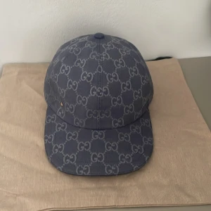 Dubai Gucci keps blå - Snygg blå keps från Gucci med klassiskt GG-monogram över hela kepsen. Justerbar rem baktill i läder och detaljer i guld. Tillverkad i bomull och linne. Helt ny och kan diskutera om priset.