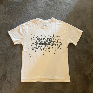 Maison Margiela T-Shirt Paint splatter - Vit t-shirt från Maison Margiela med svart grafiskt tryck och ikoniska siffror på bröstet. Klassisk passform och rund halsringning. Tillverkad i mjuk bomull och made in Italy.                          Nypris: €390 (cirka 4 300 kr) 	•	Mitt pris: 599 kr  	•	Skick: Mycket bra, sparsamt använd 	•	Storlek: S/M. Passar båda bra, Modelen på bilden är 180cm 65kg