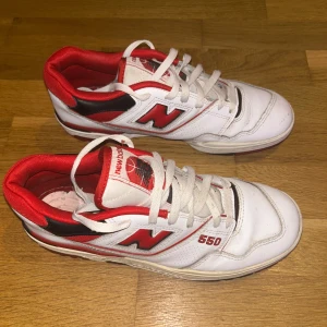 New Balance 550 vita och röda sneakers - Säljer ett par New Balance 550 sneakers i vitt och rött med svarta detaljer. Klassisk retrodesign med snörning, rund tå och platt sula. Ovandel i skinn och textil, ikonisk N-logga på sidan och NB-logga bak. Skorna kommer med originalkartong.    Nytt pris:2000kr