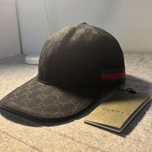 Svart Gucci keps - Skicka dm för video. Storlek ”M” Snygg svart keps från Gucci med klassiskt GG-monogram över hela kepsen. På sidan finns den ikoniska gröna och röda randen. Kepsen har böjd skärm och justerbar baksida. Materialet är slitstarkt och känns lyxigt.