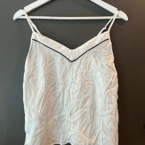 Vit satinlinne ifrån Cubus  - Jätte gulligt vit satin linne med svarta detaljer i storlek Xs ifrån Cubus. Linnet har v ringning och justerbara band. Använt en två ggr men ser ut som nytt! 