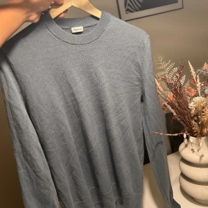 Grå stickad tröja från Filippa K - Snygg grå stickad tröja från Filippa K med rund halsringning och långa ärmar. Enkel och stilren design som passar perfekt till jeans eller chinos. Mjuk och skön kvalitet som känns lyxig mot huden.